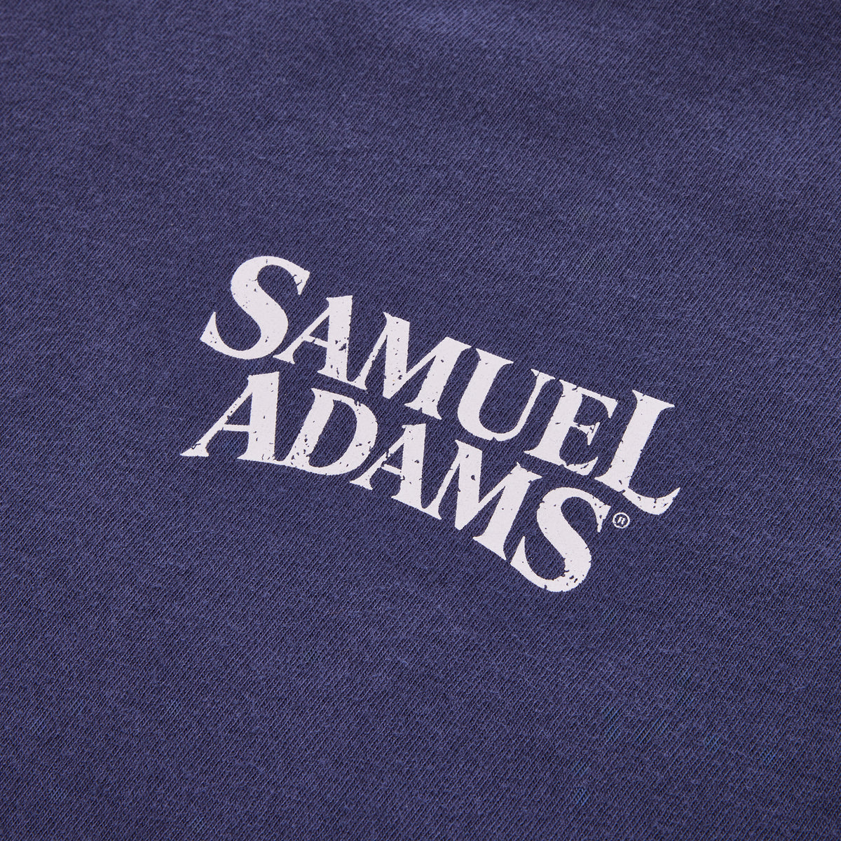 Close-up of a navy blue fabric surface with a distressed white 'SAMUEL ADAMS' logo printed diagonally across the center.