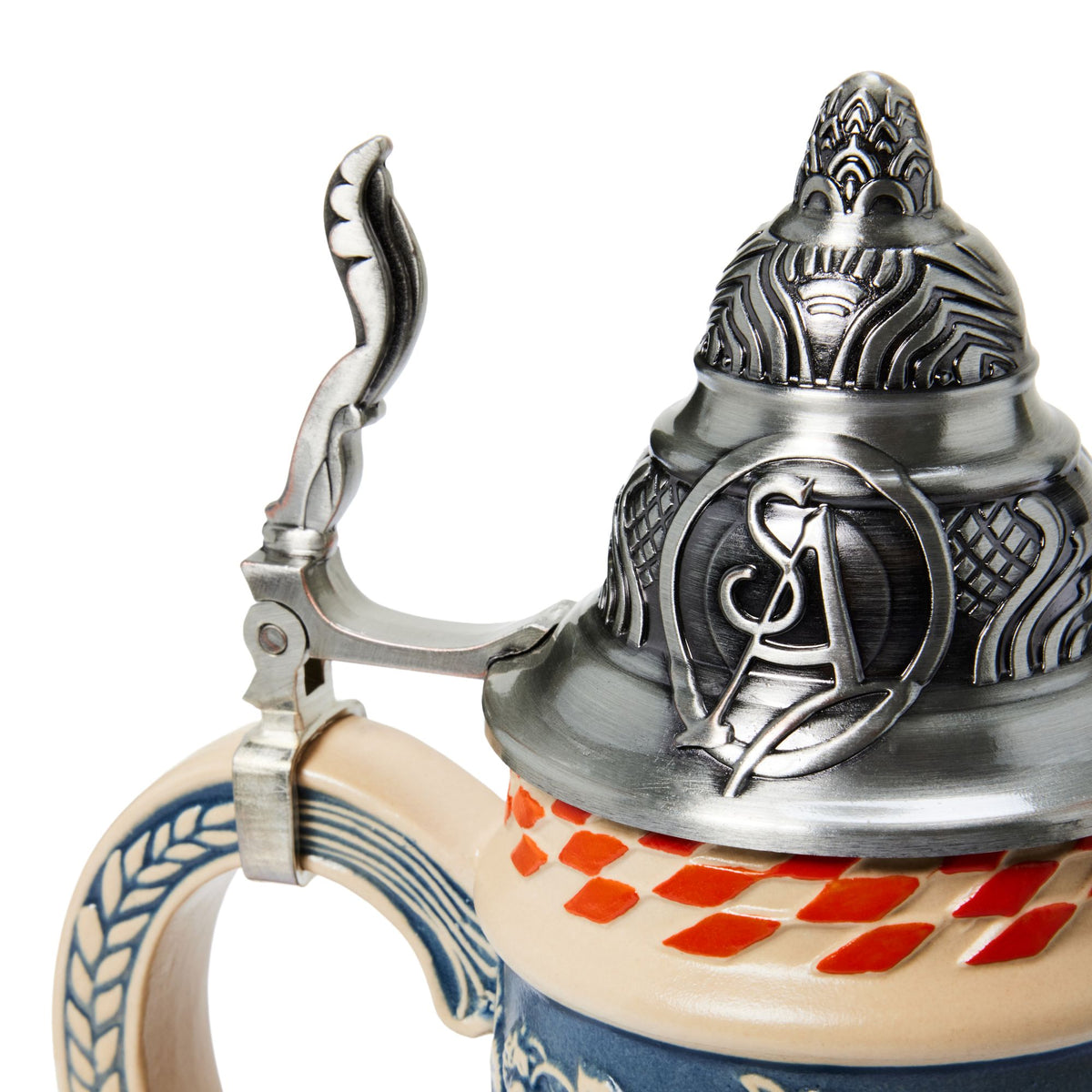 Close-up of a decorative beer stein with a silver pewter lid featuring embossed relief details and a pewter handle, attached to a beige ceramic body with blue and red diamond patterns.