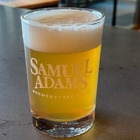 A 5.5oz Taster Glass with the classic Samuel Adams logo printed in white, filled with beer.