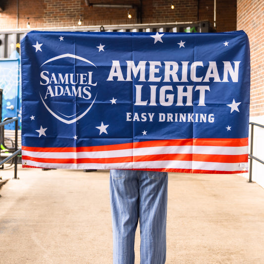 A flag with the Samuel Adams American Light logo design with red and white stripes under it and white stars over a blue background. Says "Easy Drinking" under the logos.