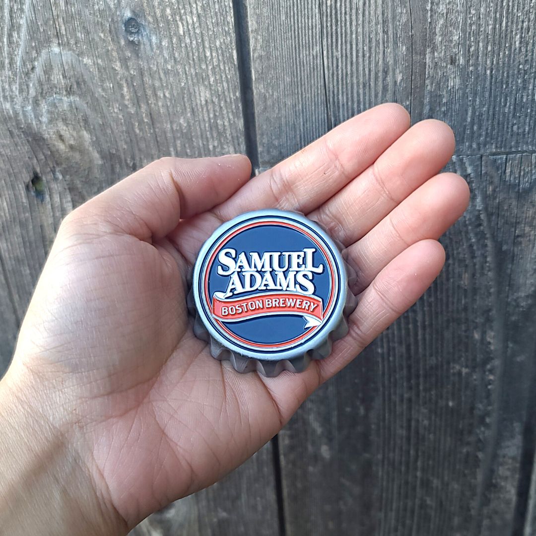 A metal bottle cap magnet with the Samuel Adams Boston Brewery logo in white and red against a navy blue background