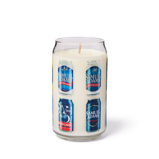 A novelty candle in a clear glass shaped like  Samuel Adams beer can, filled with white wax and featuring printed labels of  Samuel Adams Boston Lager craft beers cans around the circumference of the glass. Set on a white background