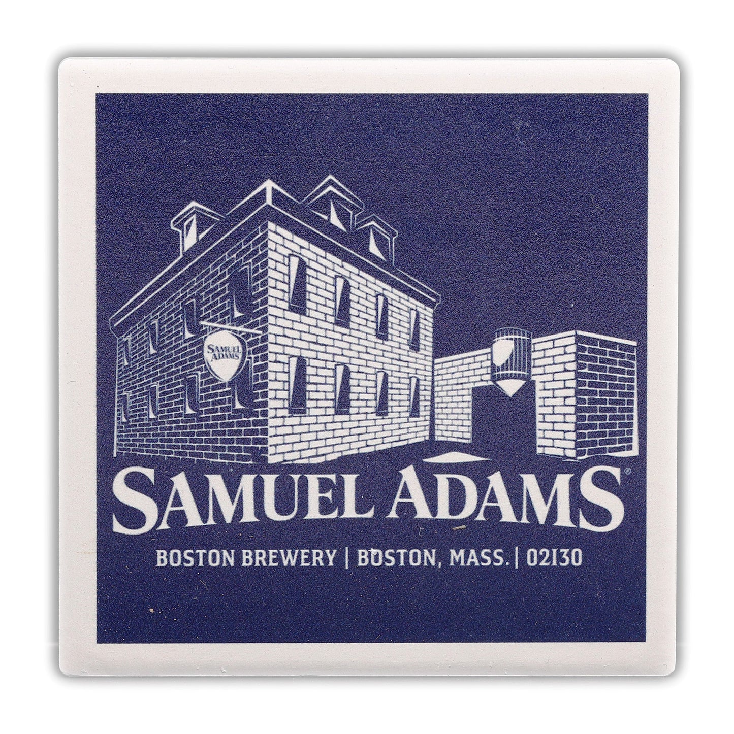 Coaster with a navy background and a white illustration of the Sam Adams Boston Brewery with the Samuel Adams logo under it and a white frame, is made of absorbent ceramic tile with a durable cork backing.