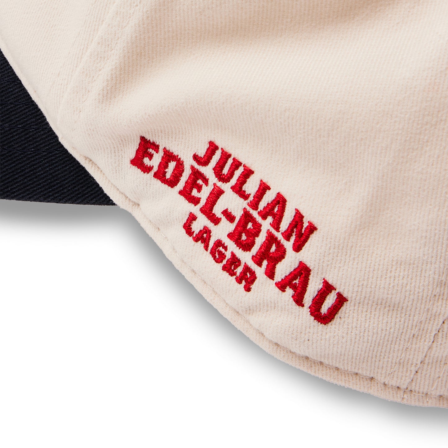 Close-up of a cream-colored fabric item with red embroidered text reading 'JULIAN EDEL-BRAU LAGER' on a white background.