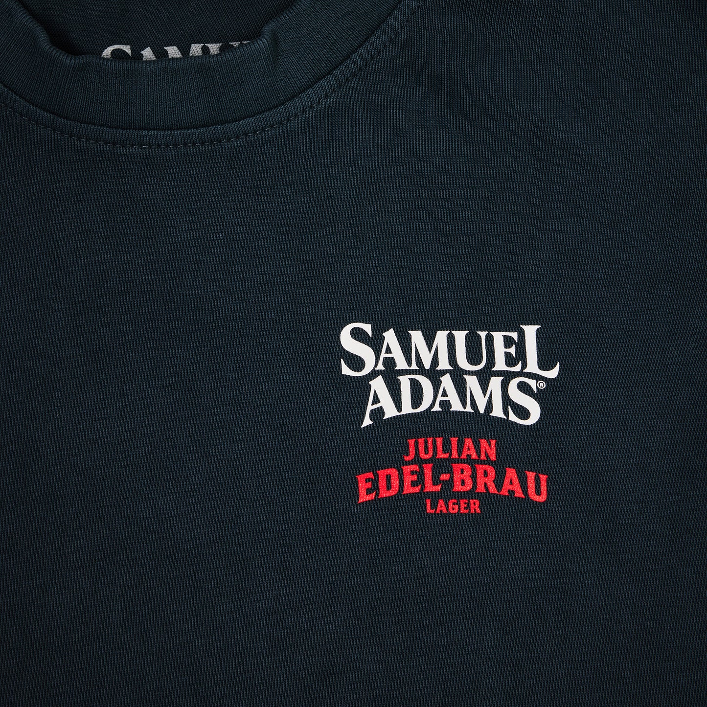 Close-up of a dark navy t-shirt featuring a white and red embroidered logo for 'Samuel Adams Julian Edel-Brau Lager' on the chest.