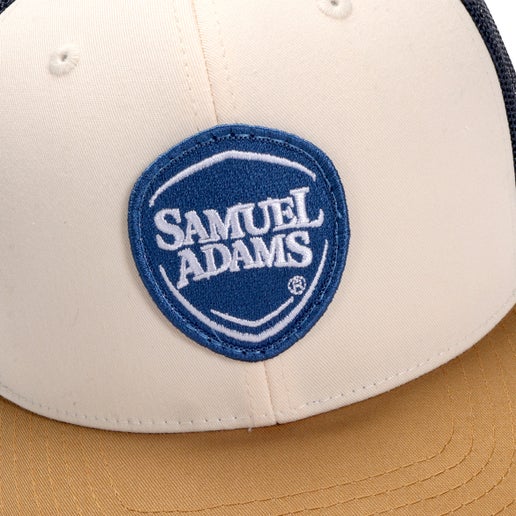 Close up of blue shield logo on Samuel Adams Navy and Gold Tri-Color Trucker Hat