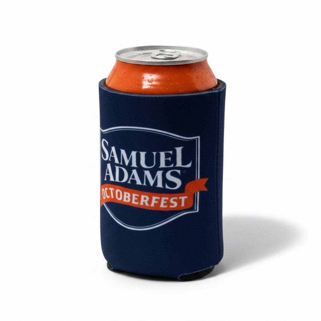 A navy blue neoprene can cooler sleeve featuring the Samuel Adams Oktoberfest logo, holding an orange beverage can on a white background.