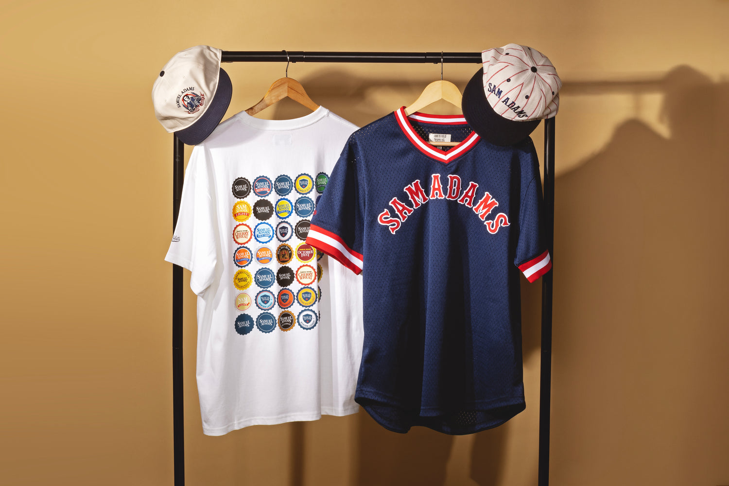 Two shirts and two caps on a rack against a beige wall