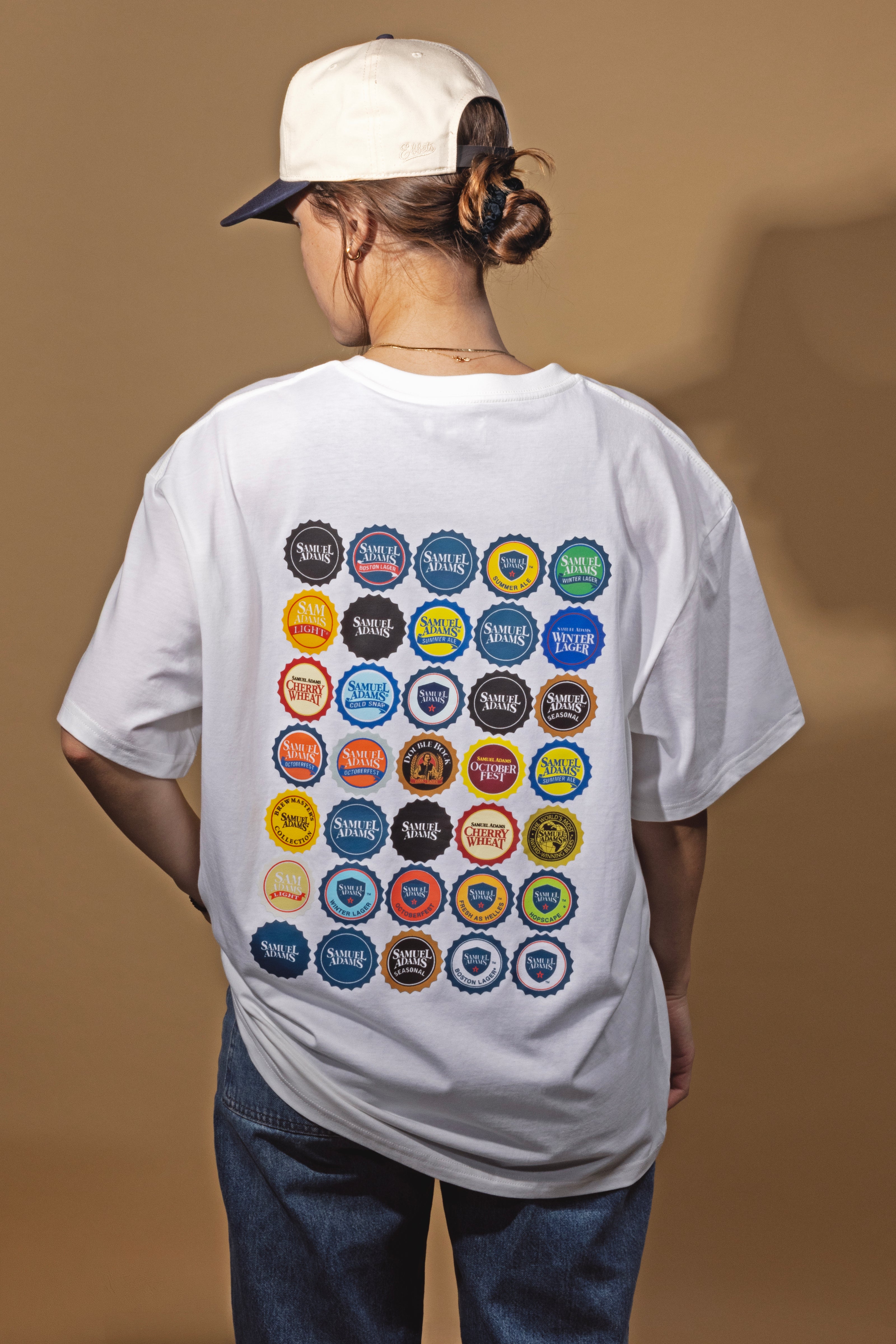 Person wearing a white t-shirt with colorful bottle cap designs on the back against a brown background
