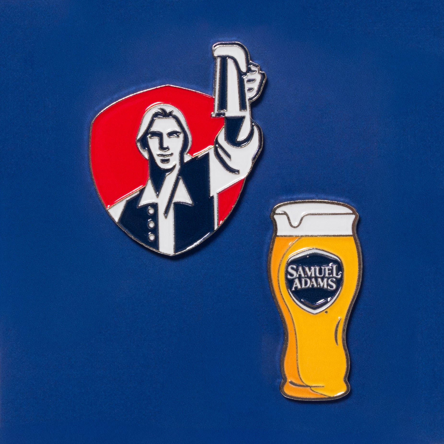 Samuel Adams golf ball marker set on blue fabric featuring Boston Lager pint glass icon and classic Samuel Adams hoist logo illustration marker
