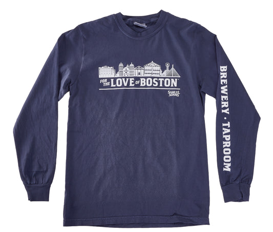 A navy blue long‑sleeve T‑shirt shown from the front. The chest displays a detailed white line‑art illustration of Boston landmarks above the phrase “FOR THE LOVE OF BOSTON,” with the Samuel Adams logo printed beneath it. The right sleeve features bold white vertical text reading “BREWERY · TAPROOM.” The shirt has ribbed cuffs and a classic crewneck collar