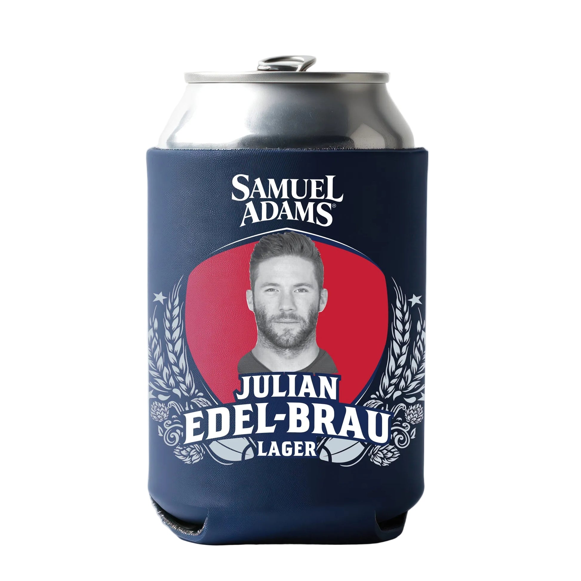 A silver beverage can encased in a navy blue can cooler with a large red oval backdrop at the center. Inside the oval is a black‑and‑white portrait of Julian Edel-Brau, framed by detailed white illustrations of barley, wheat, and hops. The Samuel Adams logo appears at the top, with bold white text reading “Julian Edel‑Brau Lager” arranged beneath the portrait