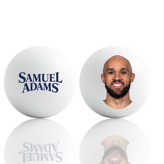 A pair of white ping pong balls displayed side‑by‑side on a reflective surface. The ball on the left shows the Samuel Adams logo in bold navy lettering. The ball on the right features a centered Derrick White headshot, printed cleanly on the smooth white surface.