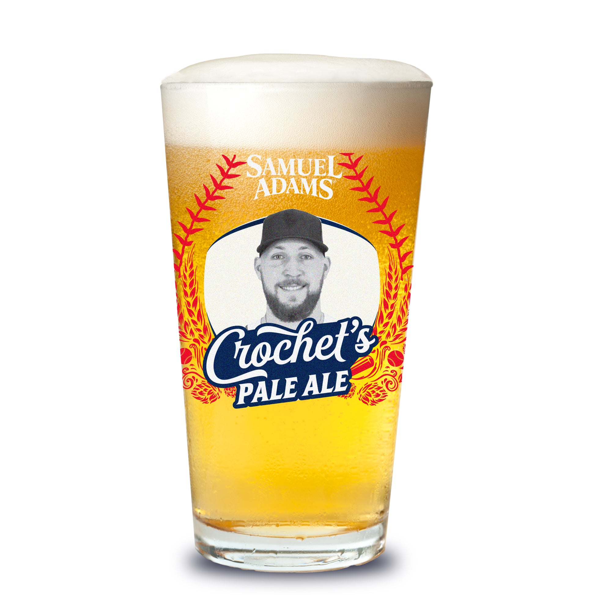 A Samuel Adams pint glass filled with golden beer, featuring a white label bordered by arcing red baseball‑style stitching; centered within the label is a black‑and‑white portrait of Garrett Crochet, with script text reading “Crochet’s Pale Ale,” and the Samuel Adams wordmark above.