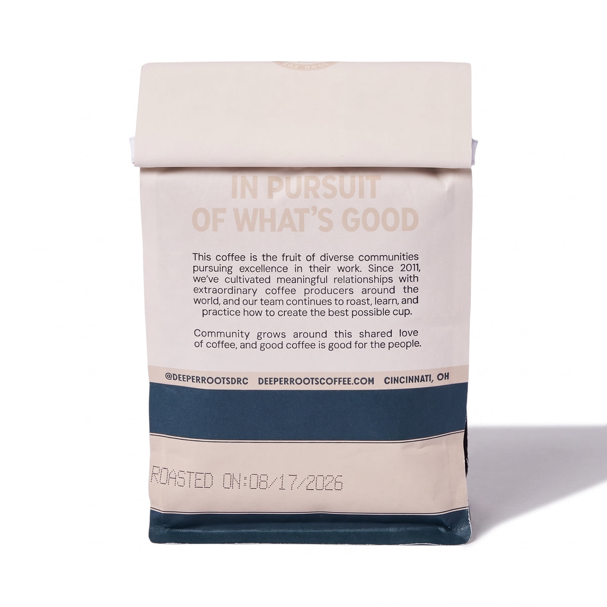 A paper coffee bag from Deep Root Coffee stands upright on a white background. The bag is primarily a warm cream/beige color with a dark navy blue band near the bottom and printed text on the front and back.