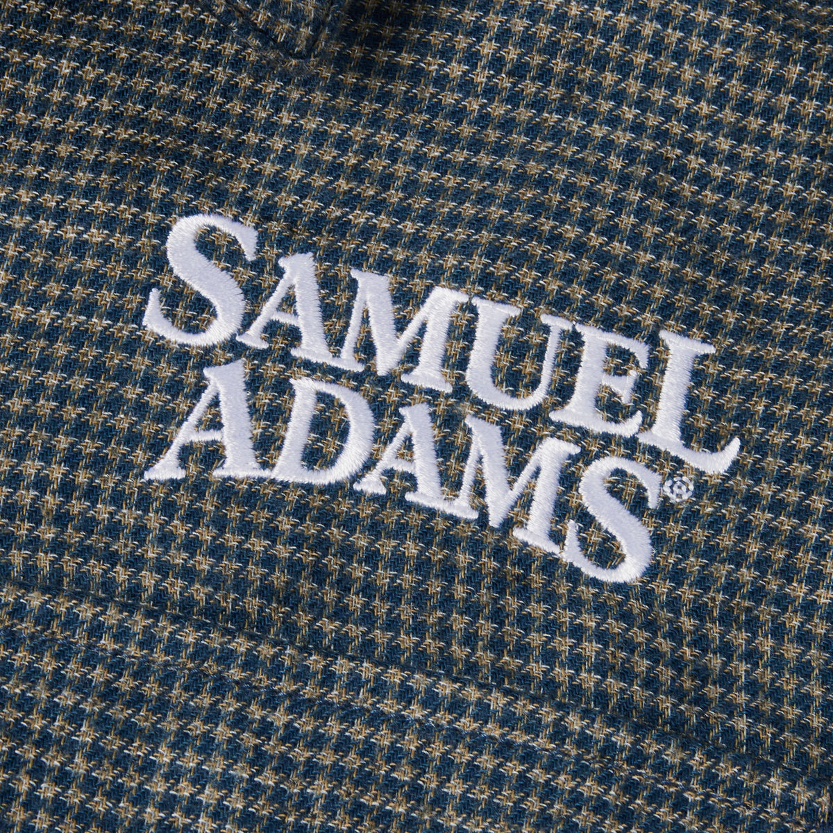 Close-up of a textured blue and tan houndstooth fabric with white embroidered 'SAMUEL ADAMS' lettering.