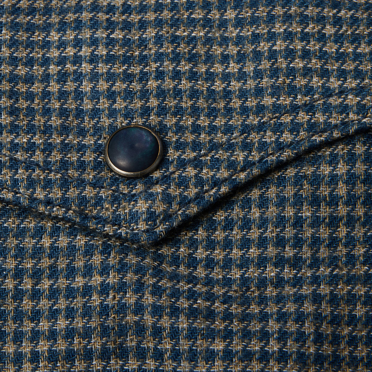 Close-up of a blue and beige houndstooth fabric with a dark metal snap button.