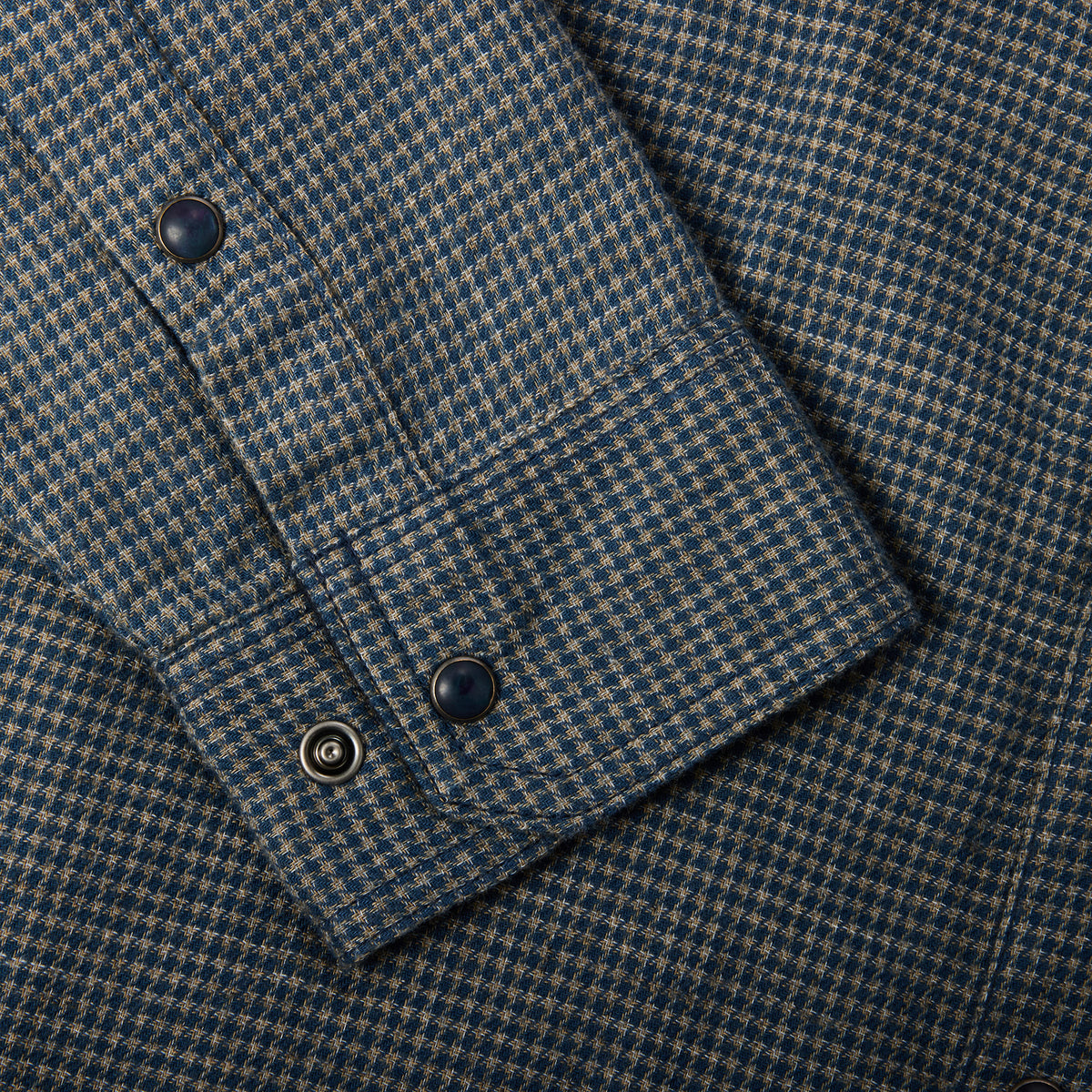 Close-up of a blue and beige houndstooth patterned fabric, showing a cuff with dark buttons.