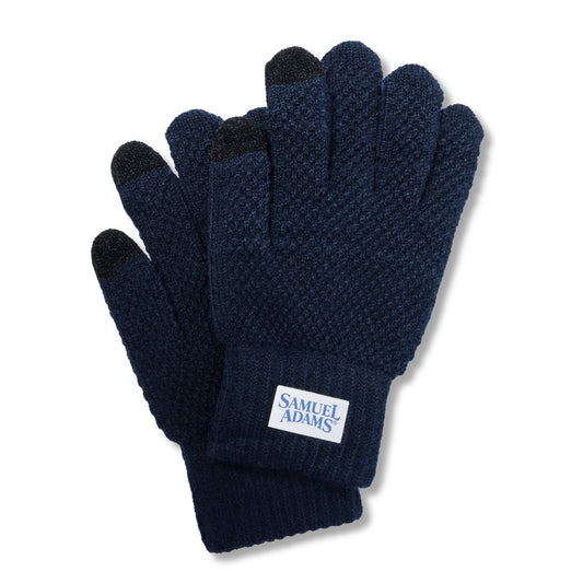 A pair of navy blue knit gloves with black fingertips and a white brand label reading 'SAMUEL ADAMS' on the cuff, shown on a white background.