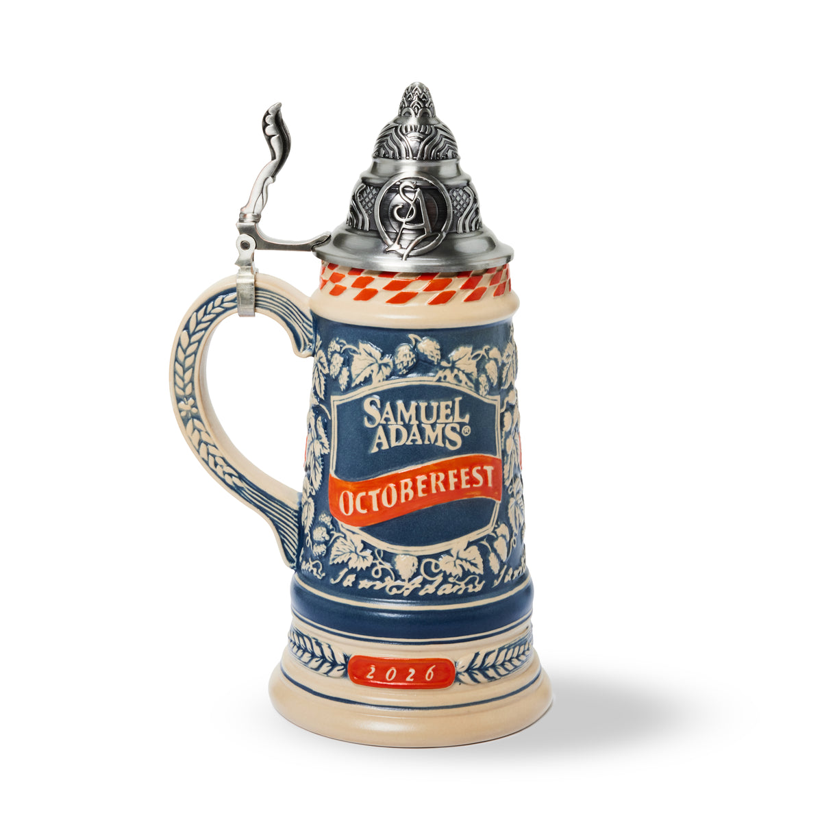 A ceramic Oktoberfest stein by Samuel Adams featuring a blue and white patterned body, a orange and white checkered band, a silver pewter lid with a bird topper, and '2026' printed on the base, shown on a white background.