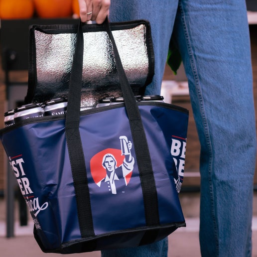 Close up of a man wearing jeans holding a navy Sam Adams-themed Cooler Bag by his side