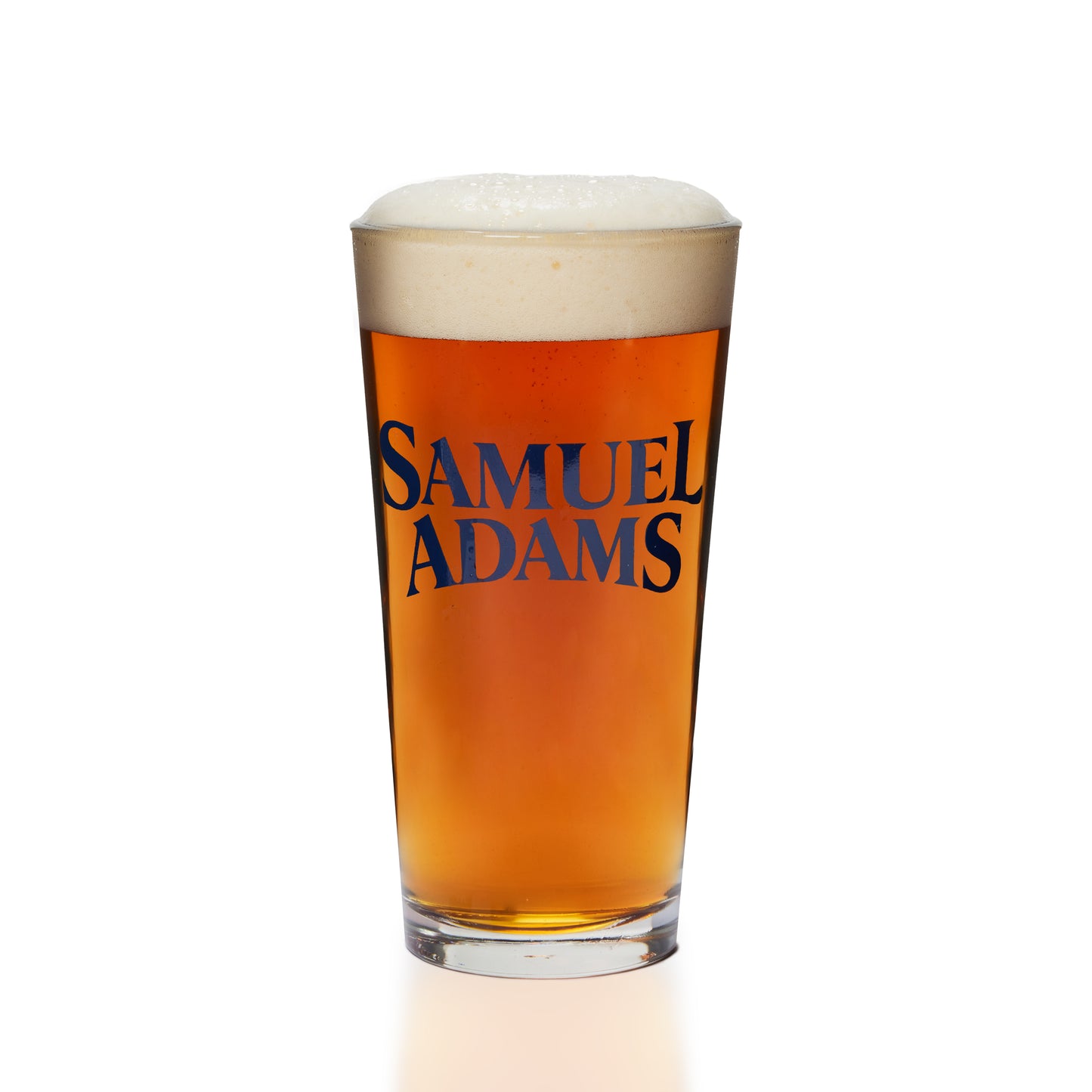 A clear pint glass filled with amber beer and topped with white foam, featuring the brand name 'SAMUEL ADAMS' printed in dark blue on the front, set against a solid white background.