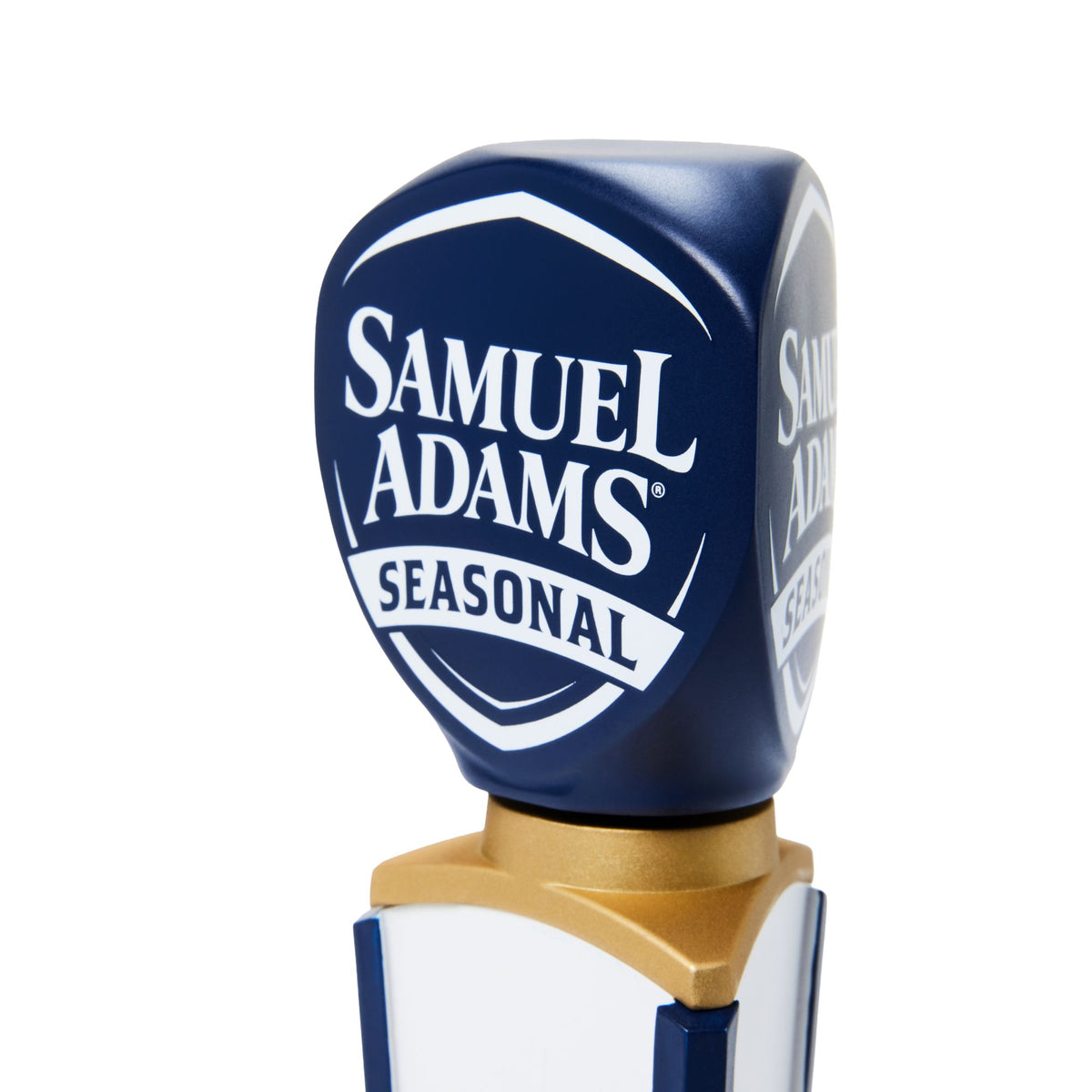 A close-up of a Samuel Adams Seasonal beer tap handle on a clean white background. The metallic cap is dark blue with white lettering, and the handle body features gold and white sections.