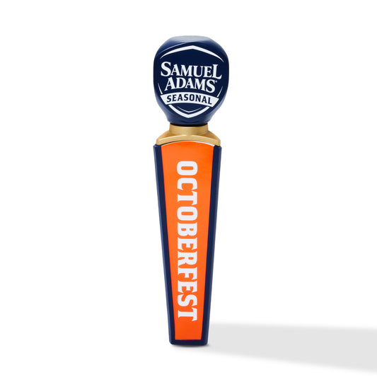 A Samuel Adams Seasonal Oktoberfest beer tap handle on a clean white background. The handle features a dark blue top with white lettering and a bright orange body with navy blue borders and white vertical text reading 'OCTOBERFEST'.
