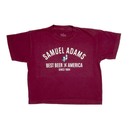 Front view of tee features writing "Samuel Adams" a small image of blue shield with Sam Adams hoisting a beer and writing "Best Beer in America Since 1984" underneath.