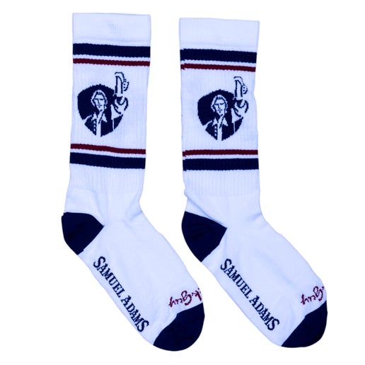 White socks with Samuel Adams written along the bottom of the foot in navy.  The leg of the sock features a navy shield with Sam Adams hoisting a beer on it.